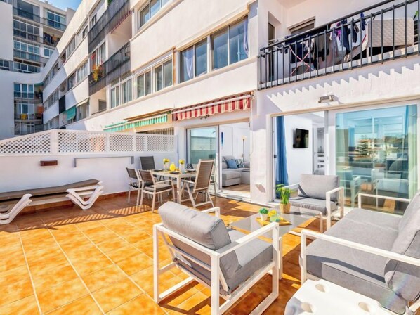 Une terrasse extérieure moderne comprenant un espace repas, des sièges et une vue sur l’intérieur du bâtiment.