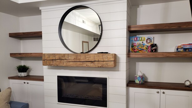 A living room with a fireplace, white paneled walls, wooden shelves, and a mirror. - Clark Suite - Millpond Inn (Clarkston)