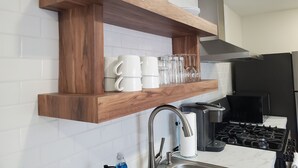 A kitchen with a wooden shelf holding mugs and glasses, a stainless steel sink, a coffee maker, and a stove. - Clark Suite - Millpond Inn (Clarkston)