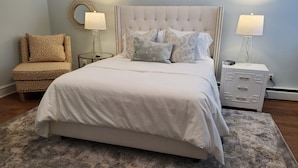 A bedroom with a large bed, two bedside tables, a chair, and a rug. - Clark Suite - Millpond Inn (Clarkston)