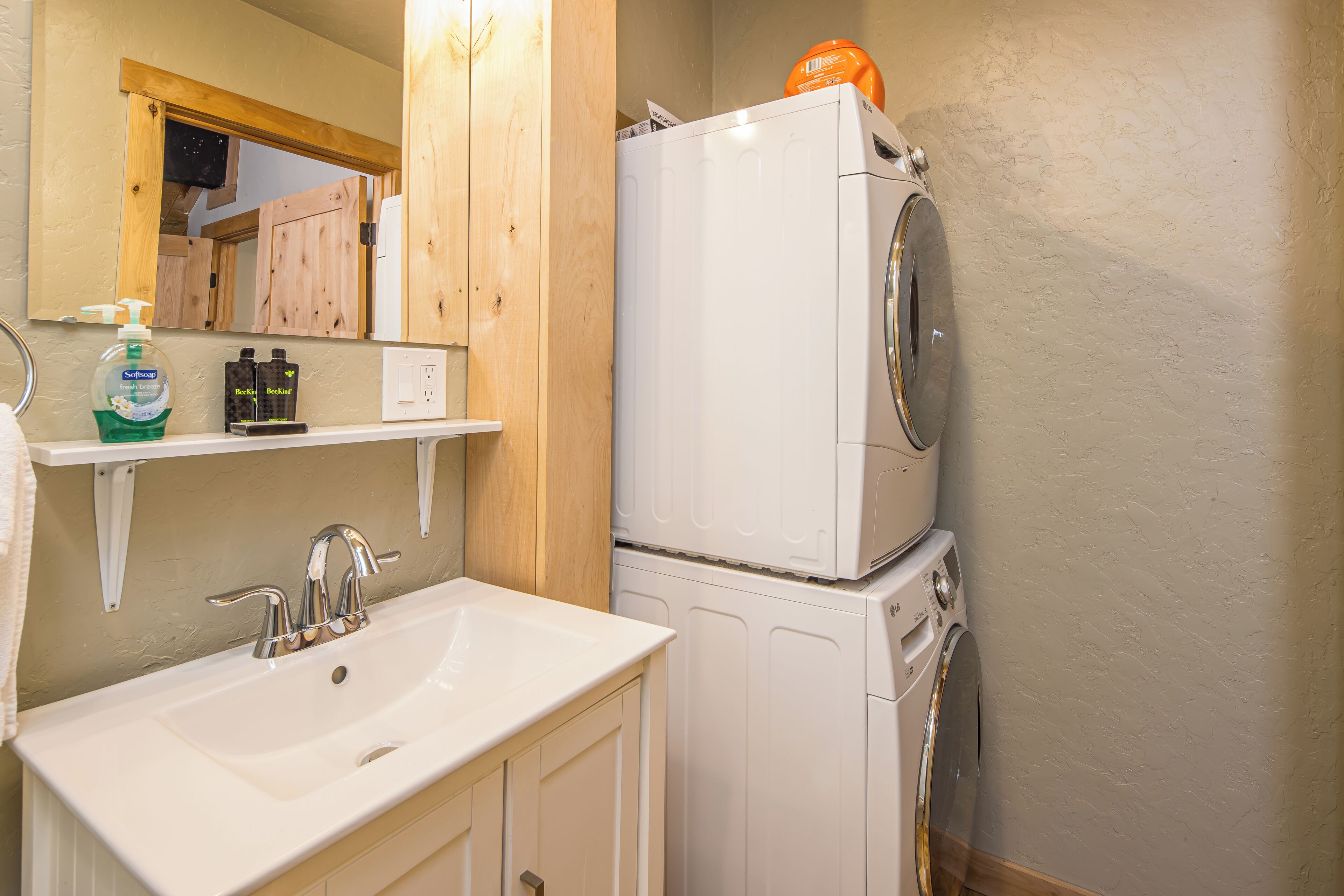 A bathroom with a sink, mirror, wooden cabinets, and a stacked washer and dryer.
