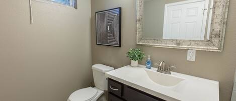 Une salle de bain avec des toilettes blanches, un lavabo surmonté d’un miroir et un tableau encadré accroché au mur.