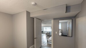 A hallway with a door leading to a living area, a vent on the wall, and a ceiling-mounted smoke detector. - NEW Renovated Guest Suite | 30 min to DIA & DEN (Brighton)