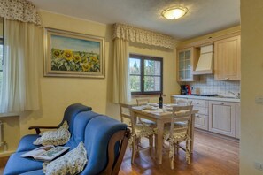 A cozy room with a blue sofa, a dining table with chairs, a kitchen area with cabinets, and a window with curtains. - Appartamento Pera shared pool, Roccastrada, Italy (Roccastrada)