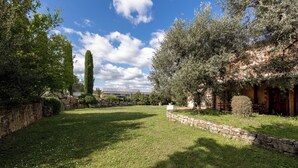 A well-maintained garden with a stone wall, a variety of trees, and a clear blue sky. - Appartamento Uva shared pool, Roccastrada, Italy (Roccastrada)