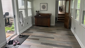 A hallway with a wooden bench, a framed picture on the wall, and a dog visible through an open door.