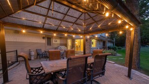An outdoor patio with a wooden table and chairs, a covered seating area, and a stone building in the background.