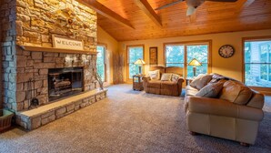 A cozy living room with a stone fireplace, a ceiling fan, and a 'WELCOME' sign above it.