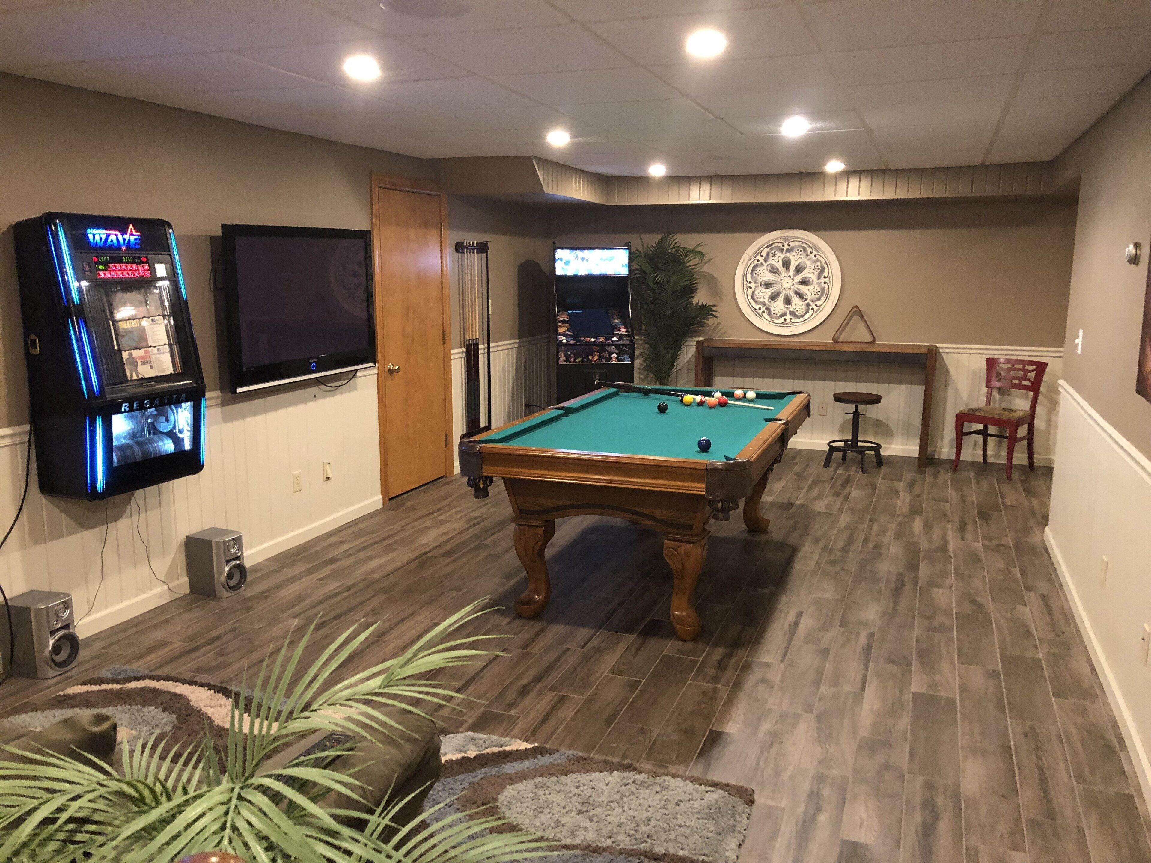 A pool table in a room with wooden flooring, a television mounted on the wall, and a dartboard on the wall.