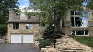 A two-story house with a stone facade, a garage, and a well-maintained front yard with a small tree and steps leading to the entrance.
