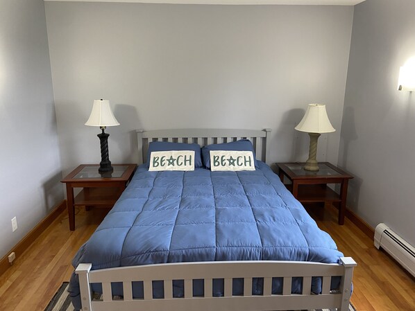 A bedroom with a bed, two bedside tables, two lamps, and two pillows with "BEACH" text.