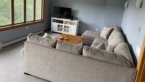 Una sala de estar con un sofá gris, una mesa de centro de madera, un ventilador de techo y un televisor sobre un mueble blanco.