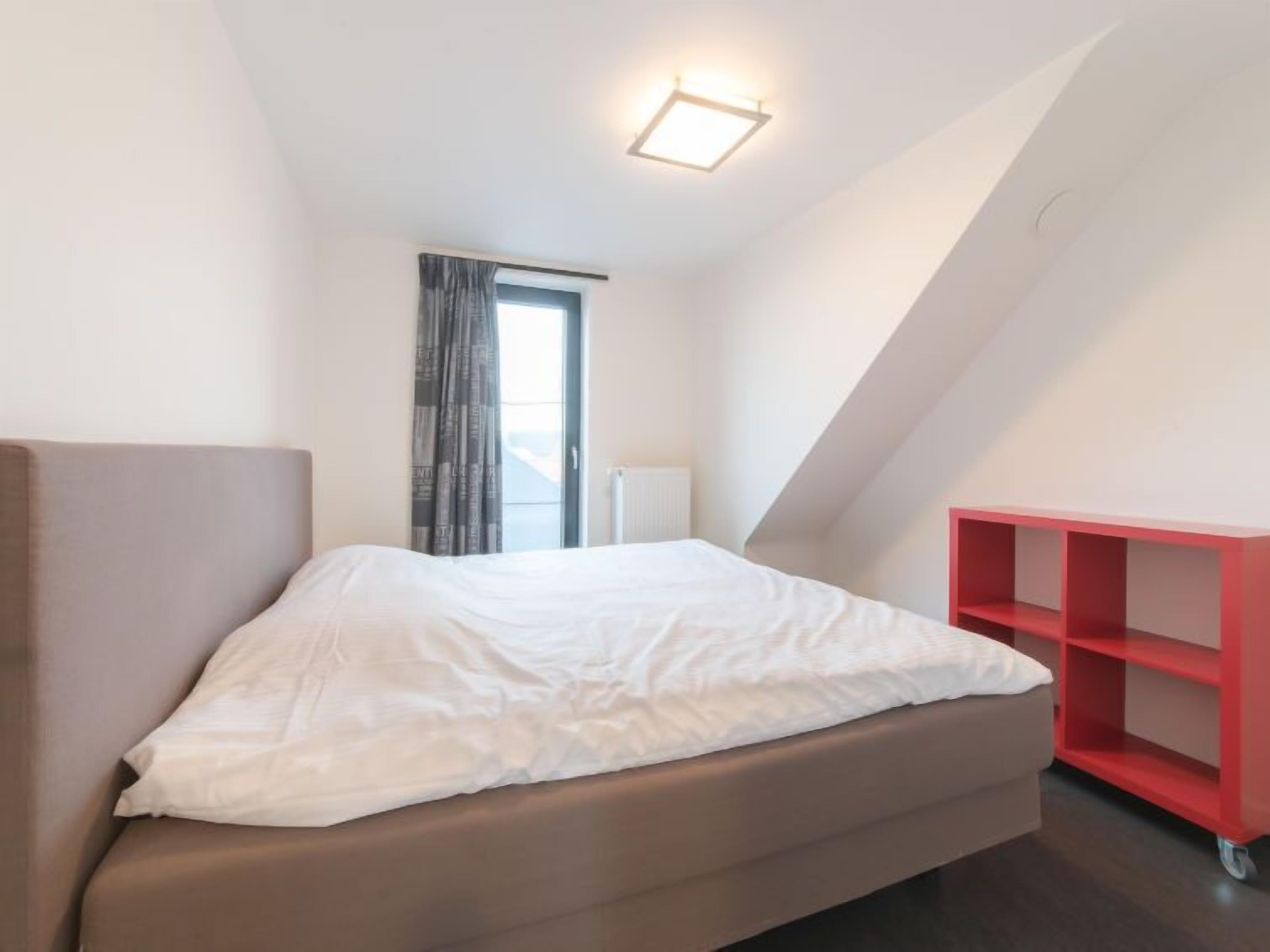 Una camera da letto moderna con un letto, un mobile contenitore rosso, una finestra con tende e una lampada a soffitto.