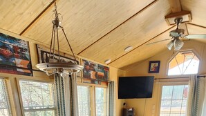 Une pièce spacieuse dotée d’un plancher en bois, d’une table à manger avec des chaises, d’un téléviseur fixé au mur et de grandes fenêtres avec des rideaux.