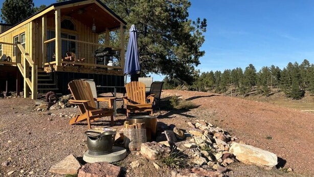 Une cabane en bois dotée d’une terrasse, d’un espace salon extérieur et d’un foyer.