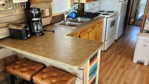 Une cuisine avec des meubles de rangement en bois, un îlot central doté de tabourets, une machine à café et un réfrigérateur.