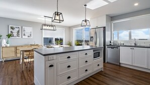 Une cuisine moderne dotée d’un grand îlot central, de meubles blancs, d’appareils électroménagers en acier inoxydable et de luminaires suspendus.