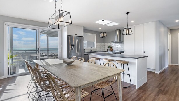 Une cuisine moderne dotée d’un grand îlot central, de meubles blancs et offrant une vue sur l’extérieur.