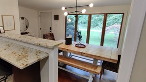 Une cuisine dotée d’un plan de travail en granit, d’une table à manger en bois et d’un banc. Une fenêtre offre une vue sur la verdure environnante.