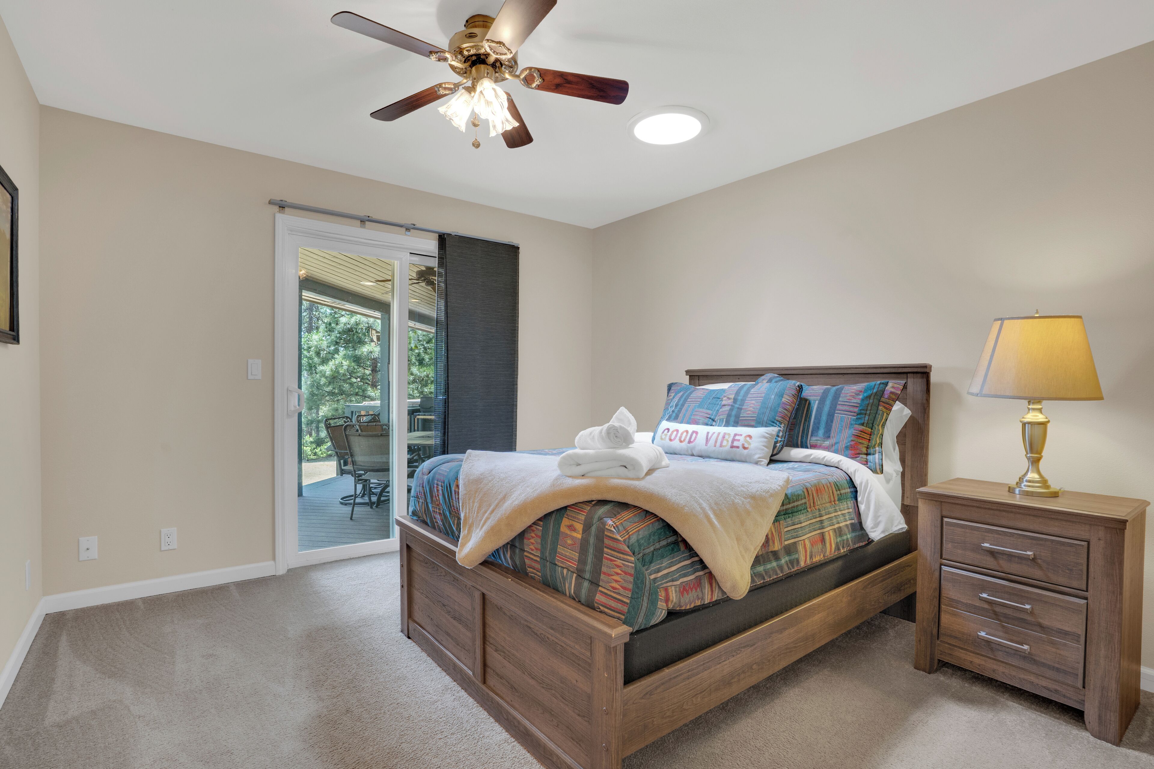 Une chambre avec un lit, une table de chevet, un ventilateur de plafond et une vue sur une terrasse extérieure, accessible par une porte coulissante.