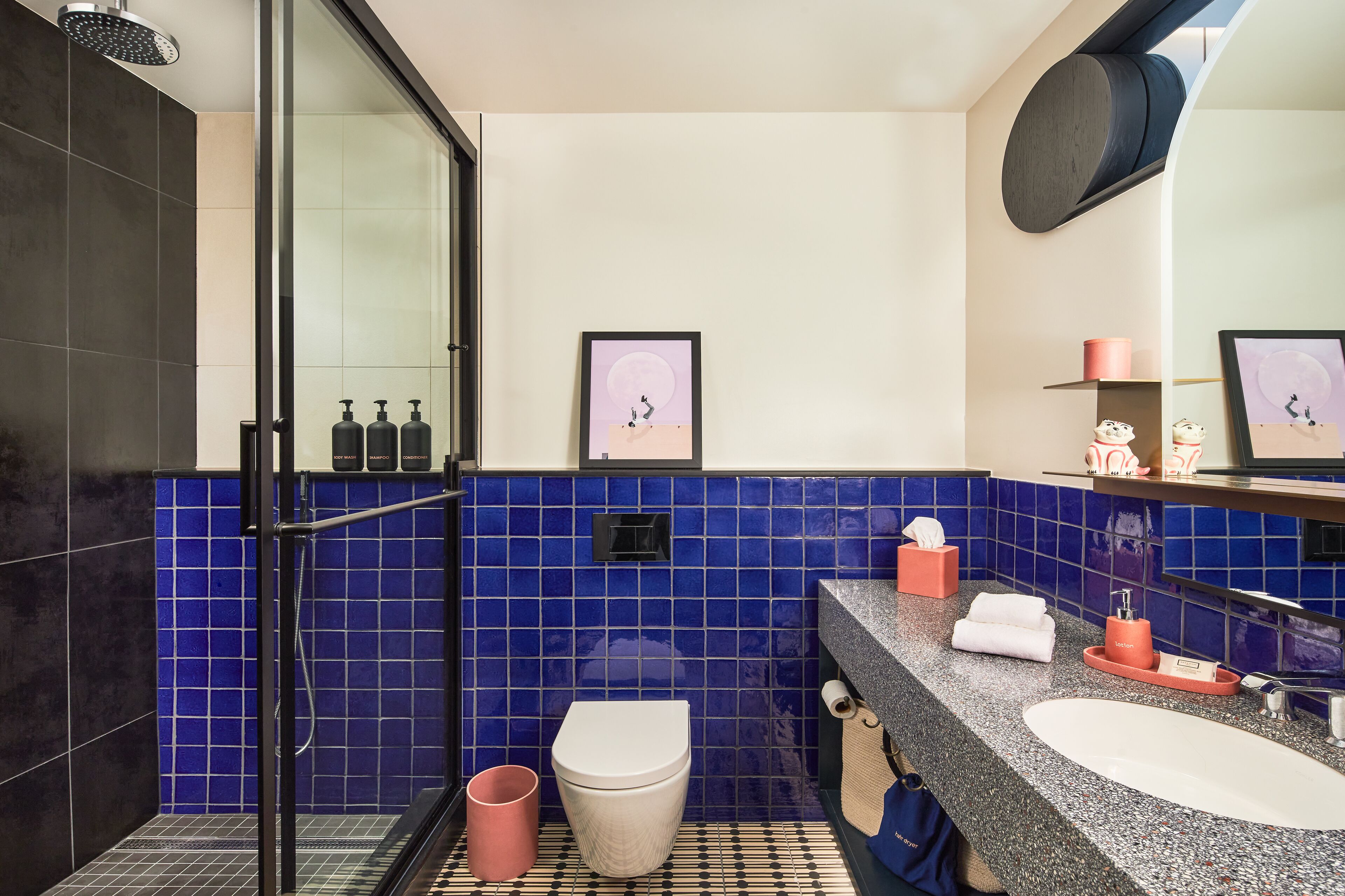 A modern bathroom with a glass shower enclosure, a white toilet, a sink with a mirror, and a blue-tiled wall.