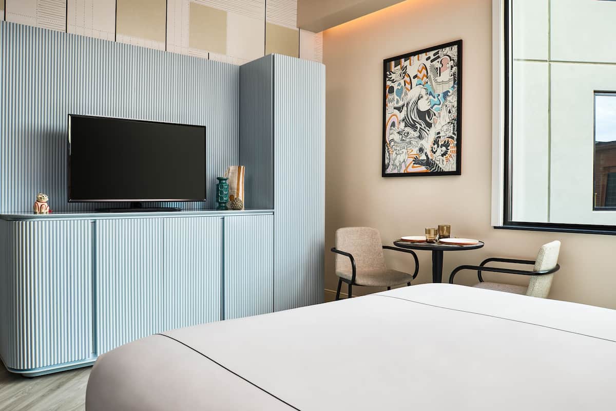 A hotel room with a large flat-screen TV on a built-in cabinet, a small table with two chairs, and a large window.