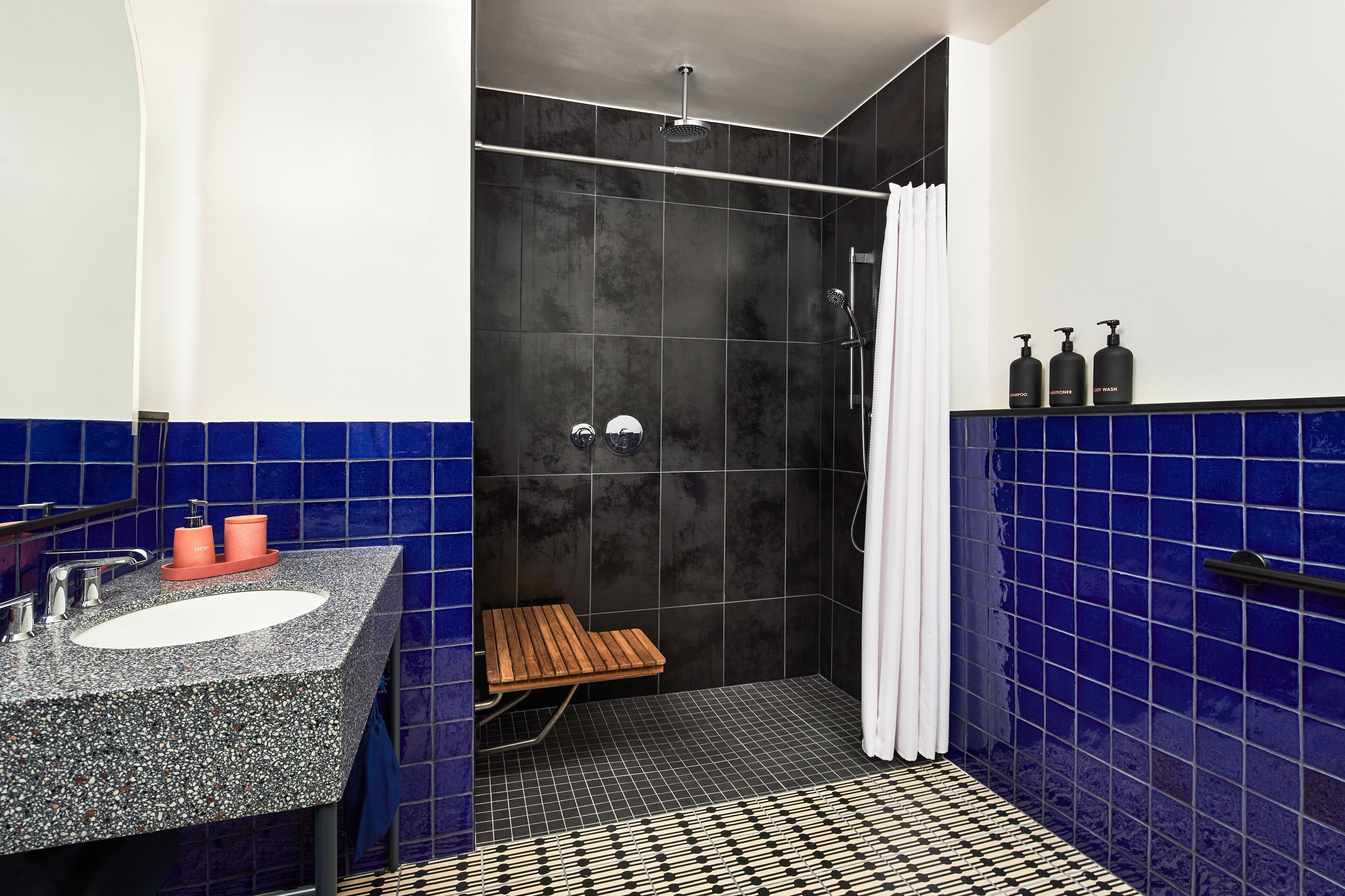A bathroom with a sink, shower, and a small wooden bench.