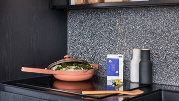 Una cocina con encimera negra, una olla rosa con tapa, una caja de Catbird Spice Rack y dos recipientes de especias.