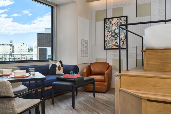Un salón moderno con un sofá, un sillón de cuero marrón, una mesa de comedor con platos y vasos, y un ventanal con vistas a la ciudad.
