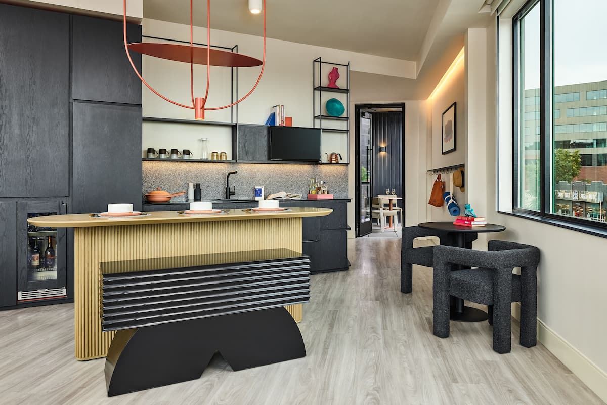 A modern kitchen with a central island, dark cabinetry, and a view of the city through large windows.