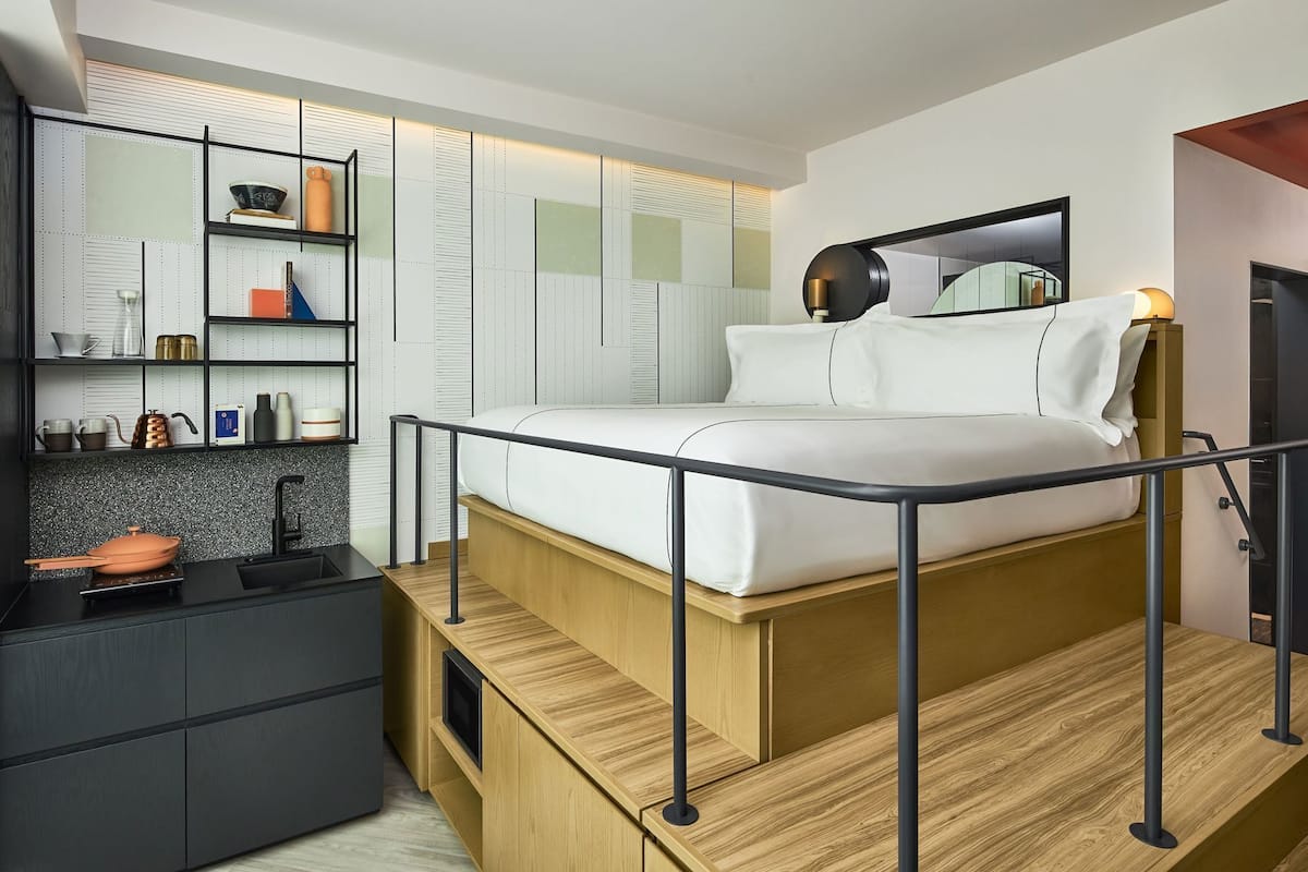 A modern bedroom with a bed, a small desk, a mirror, and built-in shelving.