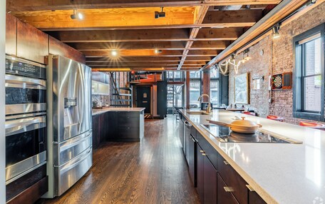 A modern kitchen with stainless steel appliances, wooden flooring, and a brick wall.