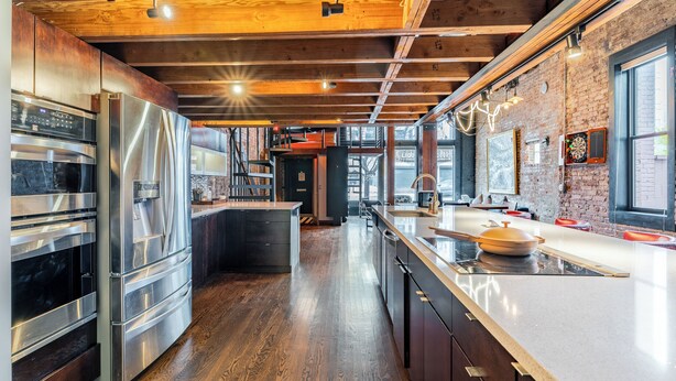 Una cocina moderna con electrodomésticos de acero inoxidable, suelo de madera y pared de ladrillo.