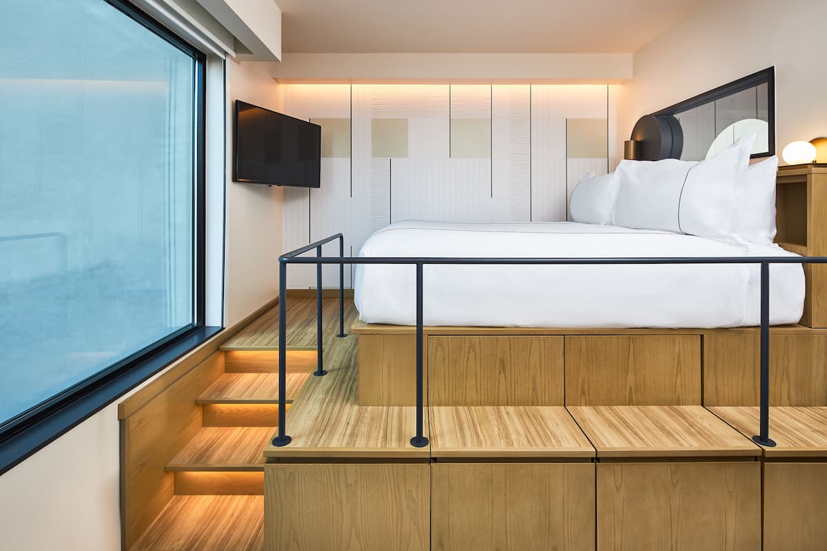 A modern hotel room with a bed, a TV mounted on the wall, and a window with a view.