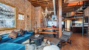 Un loft amplio con paredes de ladrillo visto, una cama alta, un comedor y un cuadro grande.