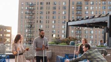 A pool table with four people playing, surrounded by outdoor seating and a cityscape in the background.