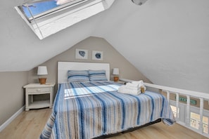 A bedroom with a sloped ceiling, a bed with striped bedding, two wall-mounted lamps, and a view of the sky through a skylight. - Odysea: Hampton Beach Getaway – Seafood, Music & Waves Await! (Hampton)