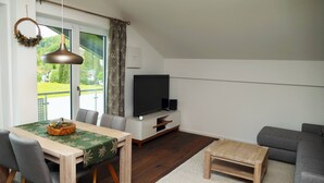 A modern living room with a dining table, grey sofa, and a flat-screen TV.