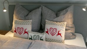 Un lit avec une literie grise et deux coussins décoratifs ornés de motifs de rennes et de cœurs.