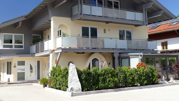 A multi-story building with balconies, a stone sculpture, and a well-maintained garden.