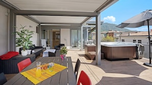 An outdoor patio with a table, chairs, a hot tub, and a covered seating area.