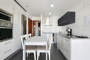 Una cocina moderna con armarios blancos, electrodomésticos de acero inoxidable y un comedor con mesa y sillas blancas.