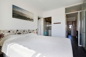 Un dormitorio con cama, un cuadro, un baño con toalla y un pasillo que conduce a una cocina.