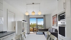 A modern kitchen with a dining area, large windows, and a view of palm trees. - Apartment "Casa Raquel 1" with Sea View, Pool, Wi-Fi & Terrace (Costa Antigua)