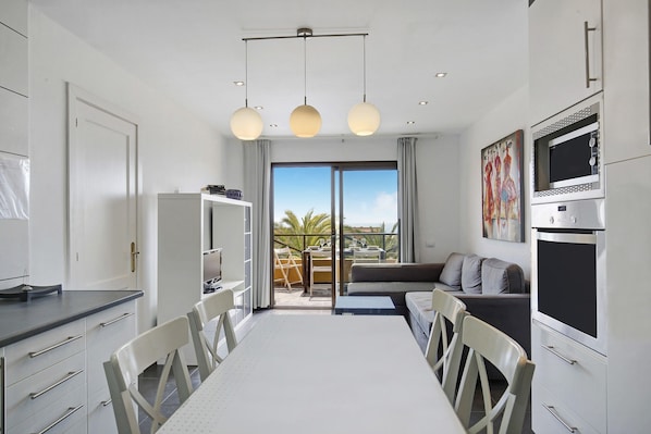 Una cocina moderna con comedor, ventanas amplias y vistas a palmeras.