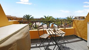 A balcony with a table and chairs, a metal railing, and a view of buildings and palm trees. - Apartment "Casa Raquel 1" with Sea View, Pool, Wi-Fi & Terrace (Costa Antigua)
