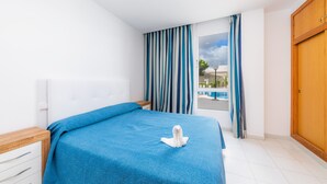 A hotel room with a bed, a wooden wardrobe, a window with curtains, and a view of a swimming pool.