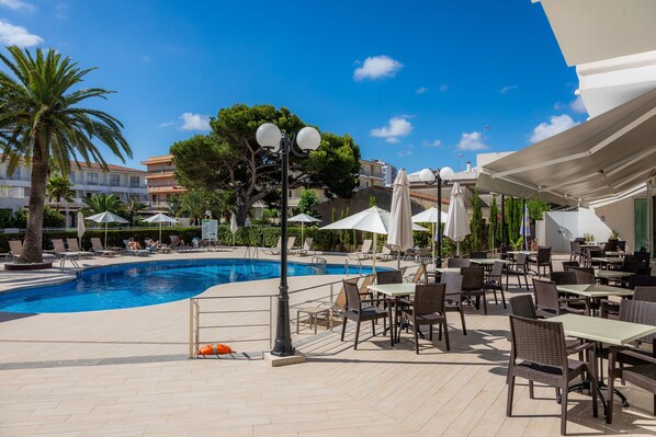 A poolside area with lounge chairs, umbrellas, and dining tables.