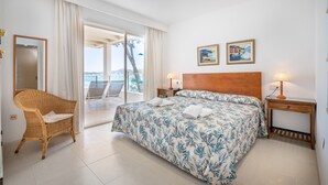 Ein Schlafzimmer mit einem Bett, einem Korbsessel, einem Holzkopfteil, zwei Nachttischlampen und einem Balkon mit Blick.