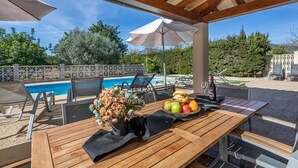 A wooden table with a vase of flowers, a fruit bowl, and a bottle of wine. - Villa "Can Antich" with Mountain View, Pool, Wi-Fi, Garden & Terrace (Lloseta)
